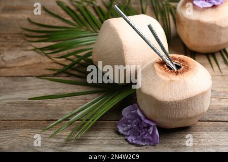 Noci di cocco fresche con cannucce da bere e fiori su tavola di legno. Spazio per il testo Foto Stock