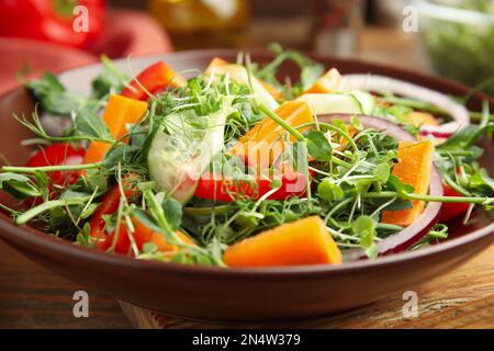 Deliziosa insalata di verdure con microgreens servita su tavolo di legno, primo piano Foto Stock