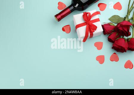 Bella scatola regalo, rose e vino su sfondo turchese, piatto con spazio per il testo. Festa di San Valentino Foto Stock