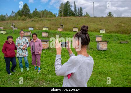 Una ragazza scatta foto su un gadget telefonico una famiglia asiatica Yakut una madre anziana con un Setra e una figlia giovane posa mano in mano contro il backgrou Foto Stock