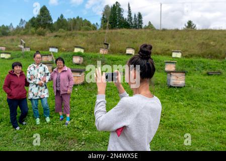 Una ragazza scatta foto su un gadget telefonico una famiglia asiatica Yakut una madre anziana con una sorella e una figlia giovane posa mano in mano contro il backgro Foto Stock