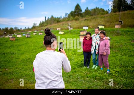 Una ragazza scatta foto su un gadget telefonico una famiglia asiatica Yakut una madre anziana con una sorella e una figlia giovane posa mano in mano contro il backgro Foto Stock