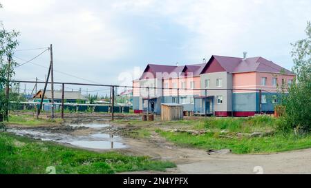 Appartamento edificio nel nord insediamento di Yakutia, suntar accanto alla strada sporca e le pozzanghere sono fatte di legno e un bagno sulla strada. Foto Stock