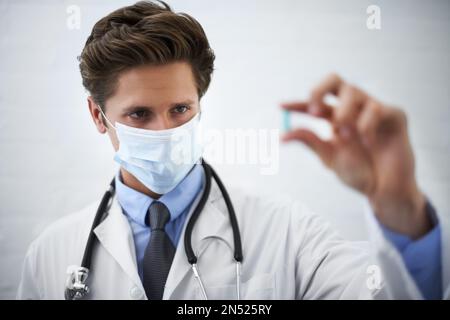 Considerando il lato. medico che indossa una maschera chirurgica che guarda una pillola che sta tenendo. Foto Stock