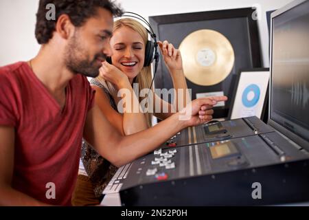 Creazione di un colpo dopo l'altro. Due giovani produttori di musica che lavorano sulla loro scrivania di mixaggio con album d'oro sullo sfondo. Foto Stock