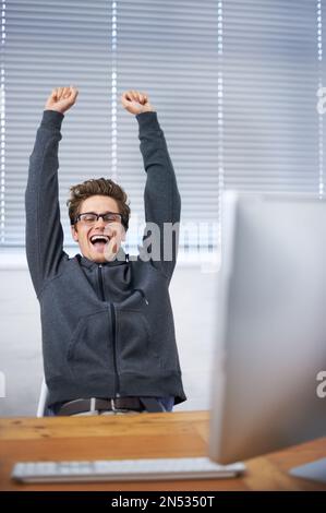 Eccitato dal suo successo. Un bel giovane che festeggia alla sua scrivania. Foto Stock