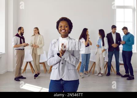 Felice giovane donna d'affari gioiosa in piedi in ufficio sullo sfondo dei suoi colleghi. Foto Stock