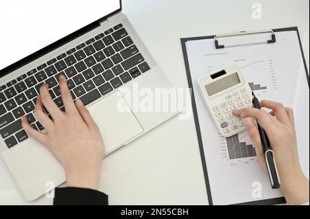 Vista dall'alto di una ragioniere professionista o di una donna d'affari che utilizza un computer portatile e una calcolatrice, che lavora alla sua scrivania. Foto Stock