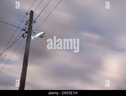 Lampada da strada inattiva su un palo nel villaggio di notte contro le nuvole e i fili del cielo. Foto Stock