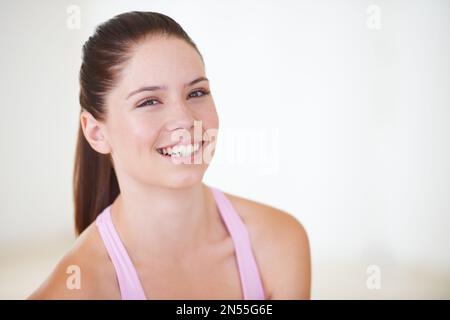 Sentirsi grandi dopo il suo allenamento. Ritratto di testa e spalle di una giovane donna attraente che indossa abiti da palestra e sorride alla macchina fotografica. Foto Stock