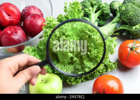 Donna con lente d'ingrandimento esplorando verdure e frutta, primo piano. Rilevamento di veleni Foto Stock