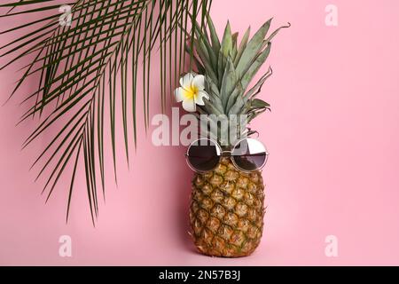 Ananas con occhiali da sole, fiori di plumeria e foglie di palma su sfondo rosa. Concetto creativo Foto Stock