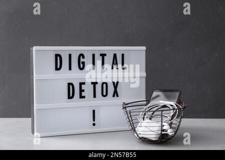 Cestino di gadget diversi e lightbox con parole DETOX DIGITALE su tavolo grigio chiaro Foto Stock