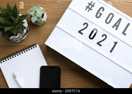 Light box con hashtag obiettivo 2021 vicino al notebook, obiettivi per il nuovo anno. Composizione piatta su tavolo di legno Foto Stock