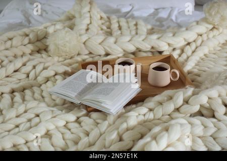 Vassoio in legno con coppe e libro su plaid a maglia bianca Foto Stock