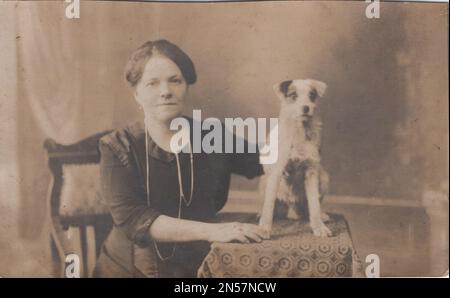 Vintage fotografia di Lady e il suo cane da compagnia / mano che tiene cucciolo / cani abbraccianti / abbracci cane / bella, intelligente, elegante signora in uno studio per scattare foto su di lei e il suo piccolo cane amorevole al 1910s. il cucciolo sembra molto spaventato. / Cane di fissaggio sotto il braccio Foto Stock