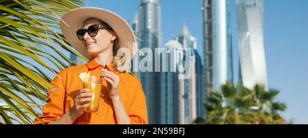 Donna sorridente e attraente in abito e cappello da sole con cocktail frullato in vacanza al Dubai Beach Resort. banner con spazio di copia Foto Stock