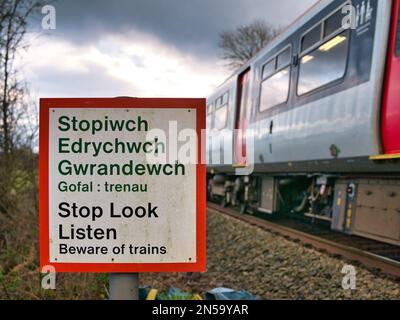 Un treno supera un segnale di avvertimento che dice "Stop Look Listen" in gallese e inglese ad un passaggio pedonale di una linea ferroviaria. In una giornata trascorsa in inverno Foto Stock