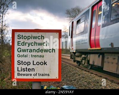 Un treno supera un segnale di avvertimento che dice "Stop Look Listen" in gallese e inglese ad un passaggio pedonale di una linea ferroviaria. In una giornata trascorsa in inverno Foto Stock