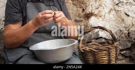 Le mani della nonna, che sbuccia le patate con il coltello, che sbuccia le patate pesanti e dure Foto Stock