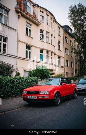 Un'Audi convertibile rossa è parcheggiata sulla strada di fronte ad alcune case. L'auto ha un colore brillante e il vicolo è tranquillo. Foto Stock