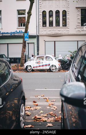 Una ripresa verticale di una Mini Cooper con Martini pubblicità sulla strada. Il cocktail è un marchio e il bianco oldtimer è retrò e vintage. Foto Stock