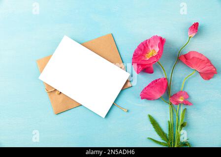 Biglietto d'auguri vuoto con bouquet di fiori di papavero rosa su sfondo blu pastello. Invito di nozze. Beffa. Giacitura piatta. Vista dall'alto Foto Stock