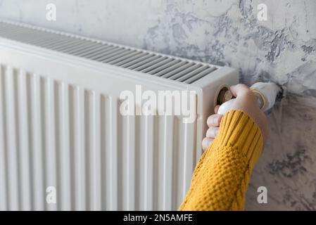 Mano maschile in maglione giallo regolazione della temperatura di comfort in casa da riscaldamento a gas di controllo. Efficienza energetica o economia in inverno concetto Foto Stock