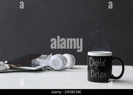 Diversi gadget e tazza con parole DETOX DIGITALE su tavolo di legno bianco Foto Stock