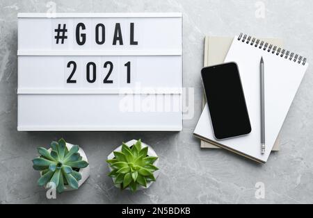 Scatola leggera con hashtag Goal 2021 vicino a notebook e smartphone moderno su tavolo grigio, piatto. Obiettivi per il nuovo anno Foto Stock