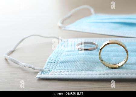 Maschere protettive e anelli da sposa su tavolo in legno. Divorzio durante la quarantena del coronavirus Foto Stock