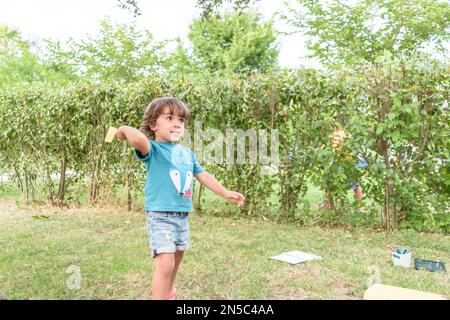 Felice ragazzo inclinazione e gettando giallo aeroplano di carta sulla luminosa giornata di sole nel campo Foto Stock