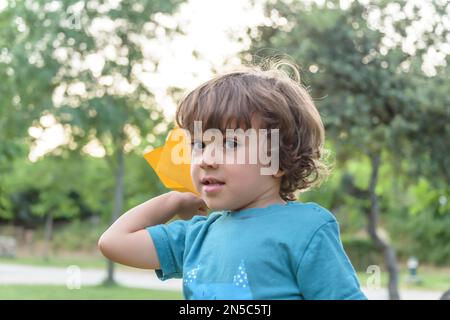 Felice ragazzo inclinazione e gettando giallo aeroplano di carta sulla luminosa giornata di sole nel campo Foto Stock