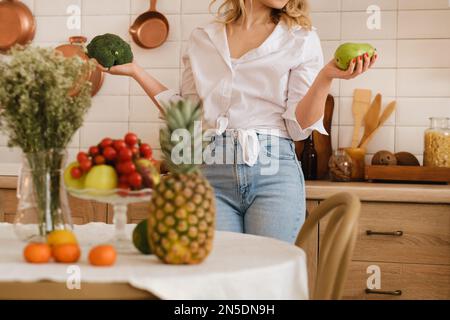 Una donna in cucina tiene in mano verdura e frutta. Verdure e frutta sono sulla tabella in fuoco molle. cucina. Foto Stock