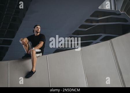 Ritratto dell'atleta del parkour seduto sul bordo della parete dopo un duro freerunning Foto Stock