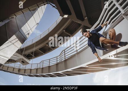 L'atleta freerunning è appeso al ponte e si sta preparando per un pericoloso salto. Parcheggio in città Foto Stock