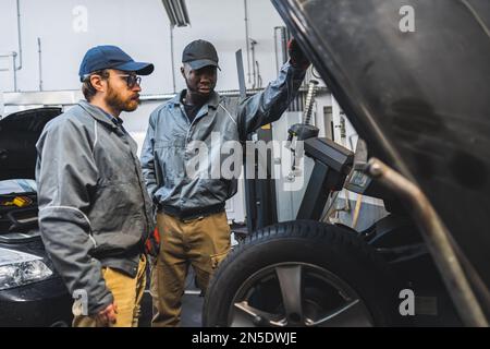 negozio di riparazione auto, due meccanici che guardano un dispositivo in un negozio di riparazione auto, medio-pieno scatto. Foto di alta qualità Foto Stock