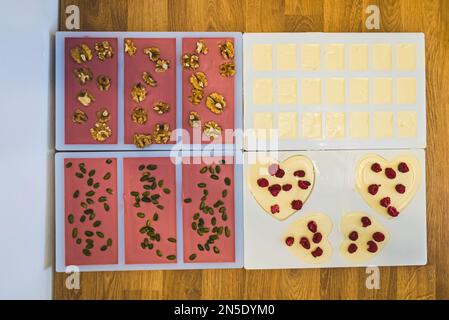 Crea cioccolato rosa e bianco con noci e frutta secca in uno stampo da bar. Foto di alta qualità Foto Stock