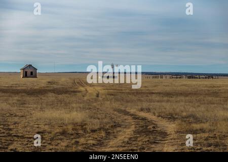 Abbandonata homefront con mulino a vento e recinzioni in legno in erba gialla pascolo nel New Mexico rurale Foto Stock