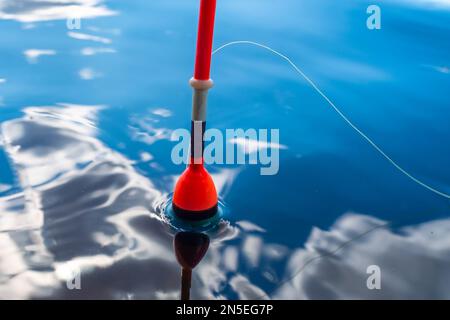 il galleggiante rosso di pesca galleggia sull'acqua in cui le nubi sono riflesse Foto Stock