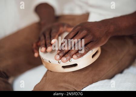 Le mani autentiche e candide dell'uomo afroamericano sul tamburello sono suonate dal ritimista durante il tempo di relax. Vita domestica multietnicità musicante maschile i Foto Stock