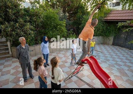 Betlemme, Cisgiordania, Palestina - 22 Luglio 2022: L'uomo Arabo in camicia arancione si alza su uno scivolo e cerca di tornare una palla bianca e blu bloccata tra tre Foto Stock