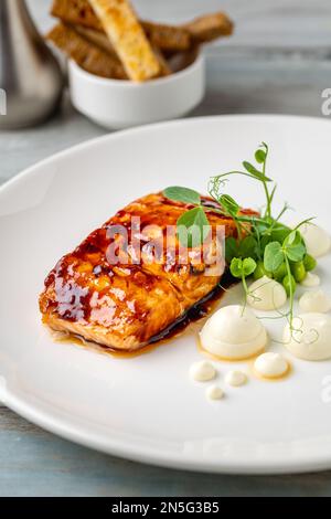 Filetto di salmone alla griglia con salse accanto su un piatto di porcellana bianca Foto Stock