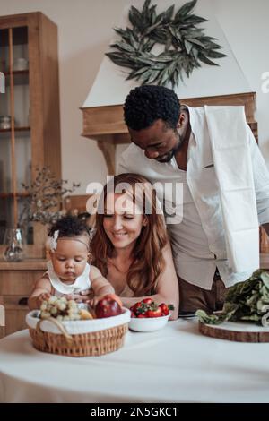 La famiglia di razza mista con il bambino bianco figlia swarthy swarthy passare il tempo insieme mattina. L'uomo afroamericano con la sua moglie giusta skinned i capretti godono healt Foto Stock