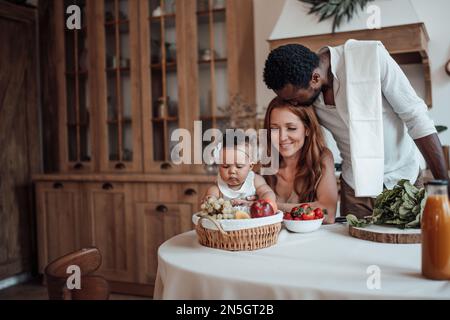 La famiglia di razza mista con il bambino bianco figlia swarthy swarthy passare il tempo insieme mattina. L'uomo afroamericano con la sua moglie giusta skinned i capretti godono healt Foto Stock