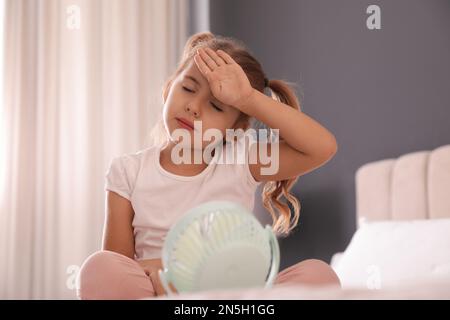 Bambina che gode il flusso d'aria dal ventilatore portatile in camera. Caldo estivo Foto Stock