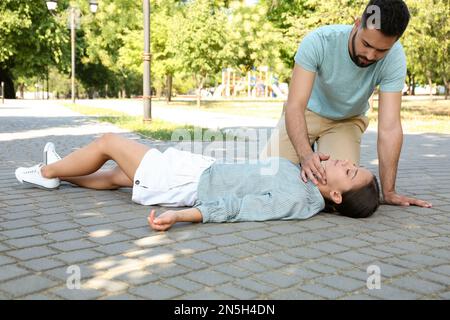 Giovane uomo che controlla il polso di una donna inconscia all'aperto. Pronto soccorso Foto Stock