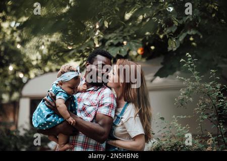 La famiglia di corse miste con una bambina dalla pelle scura passa il tempo insieme a abbracci e baci nel parco camper. L'uomo afroamericano la sua moglie e li della pelle fiera Foto Stock