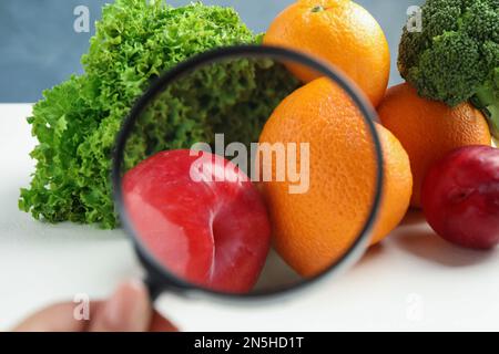 Donna con lente d'ingrandimento esplorando verdure e frutta, primo piano. Rilevamento di veleni Foto Stock