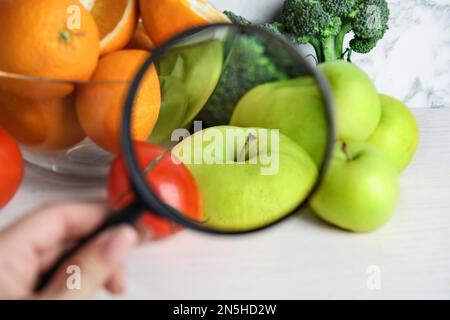 Donna con lente d'ingrandimento esplorando verdure e frutta, primo piano. Rilevamento di veleni Foto Stock